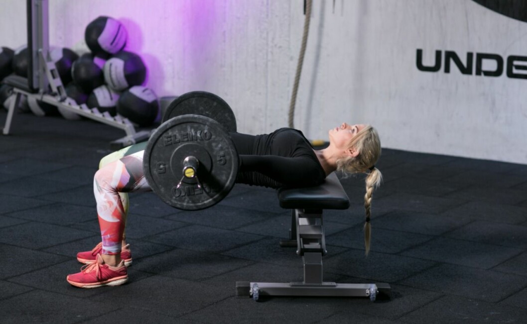 <strong>B. Rulla stången mot dig över dina ben tills den är rakt över din höft. Placera dina armbågar på bänken och händerna på stången för att hålla den stabil. Böj benen 90 grader och behåll hela fotsulan i marken. Samtidigt som du skjuter upp höften squeezar du rumpan allt vad du kan.</strong>
