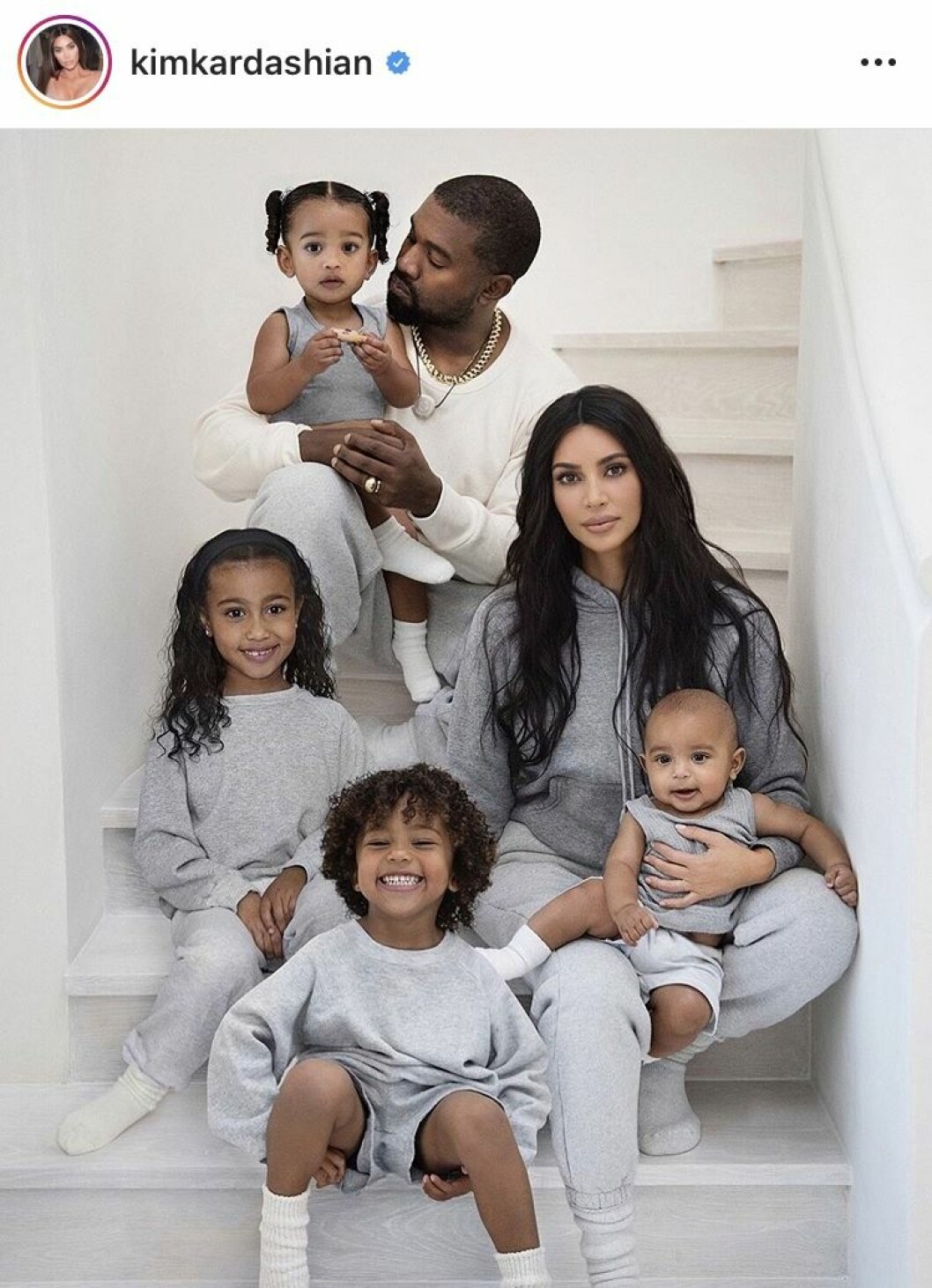 Kim Kardashian och Kanye West sitter i en trappa med alla sina barn och alla har grå mjukiskläder
