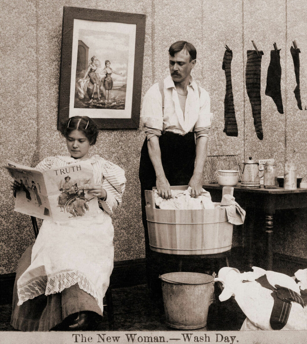 Kvinna läser tidningen samtidigt som mannen tvättar kläder.
