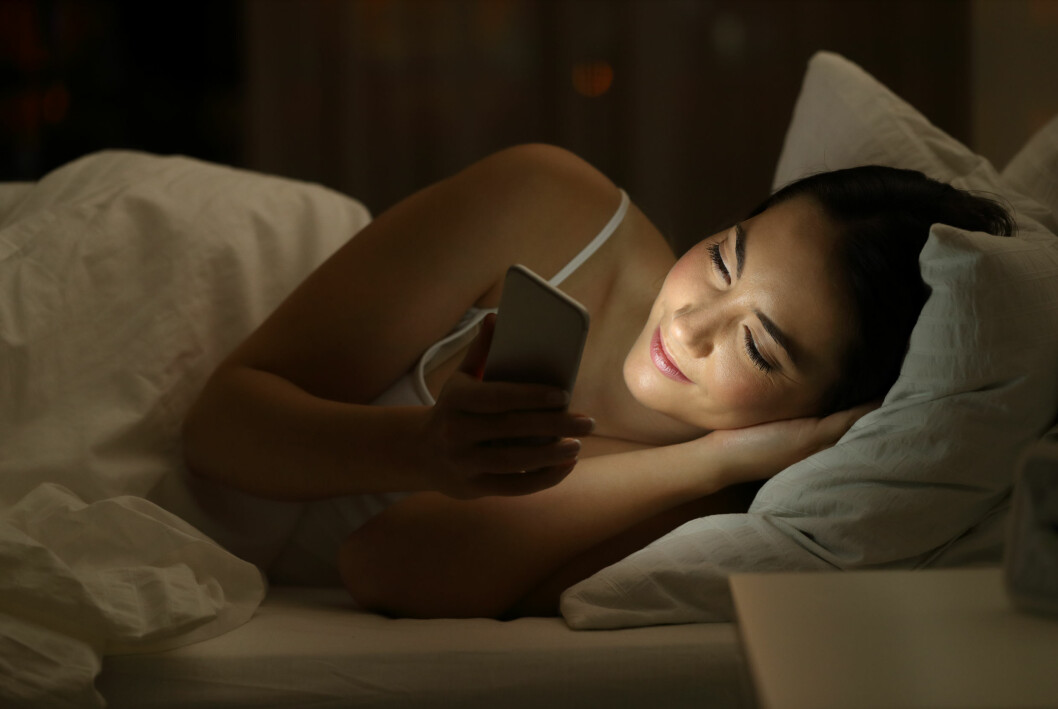 Kvinna håller på med telefonen i sängen