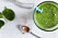 Green smoothie with banana and spinach, fresh herbs on the background, striped straw, top view