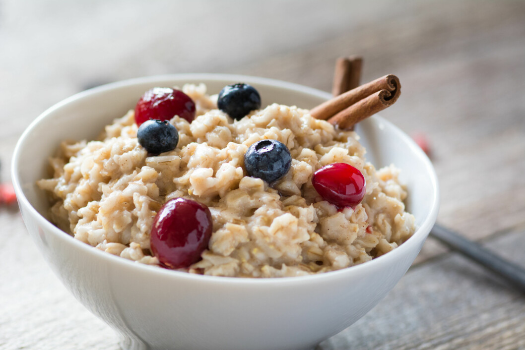 Oatmeal porridge with cinnamon, blueberries and cranberries in white bowl, close up selective focus image